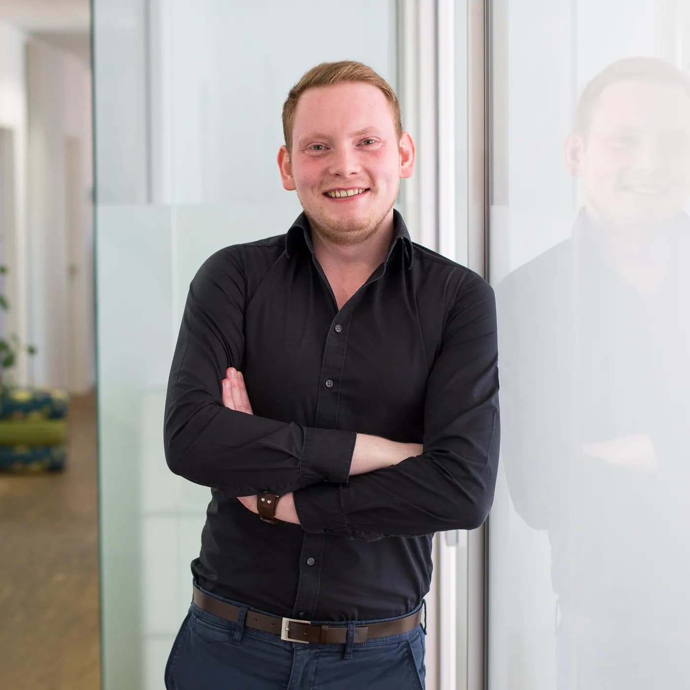 Maximilian Eckel, Gründer von BespokeCode, angelehnt an eine Glasfront in einem hellen Raum.