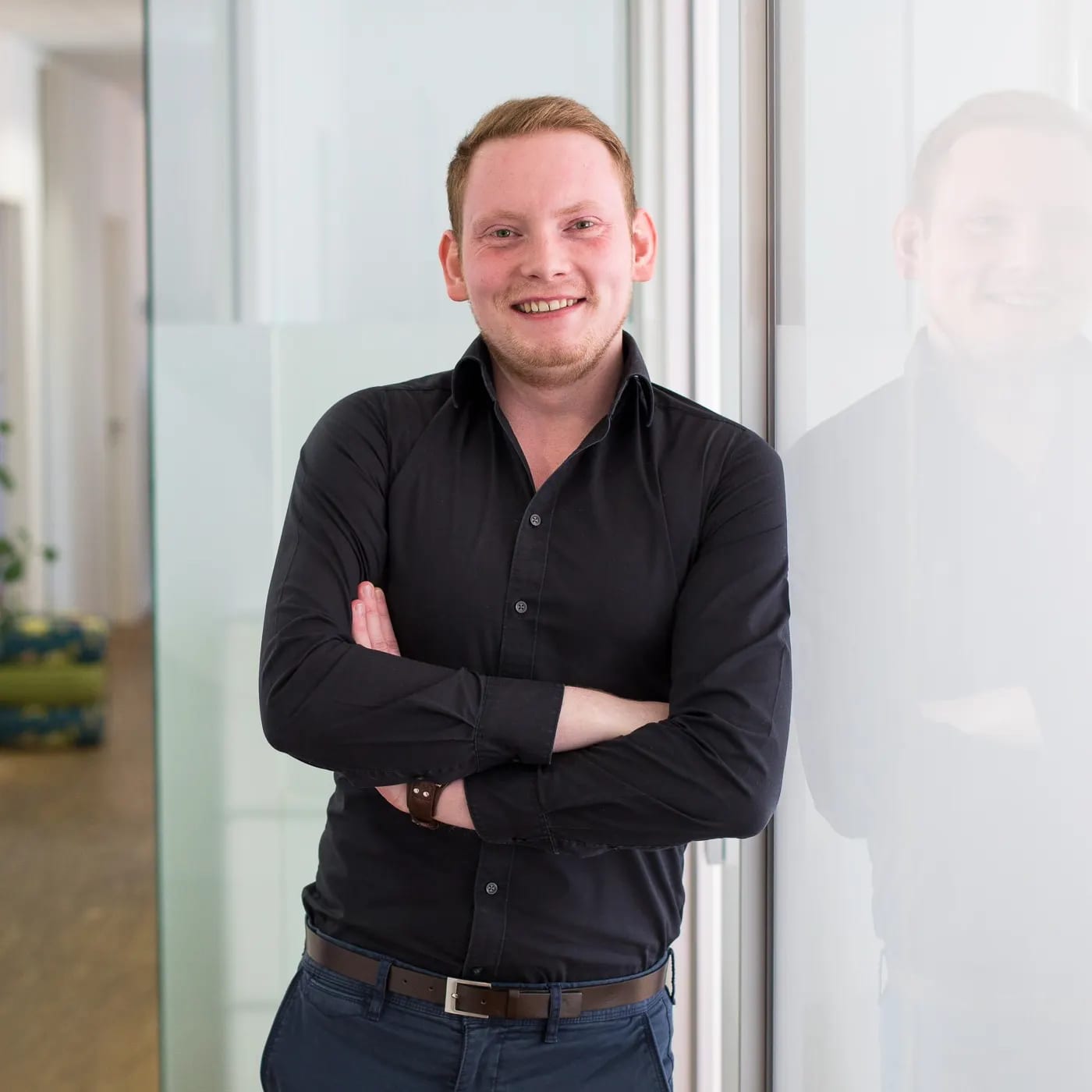 Maximilian Eckel, Gründer von BespokeCode, angelehnt an eine Glasfront in einem hellen Raum.